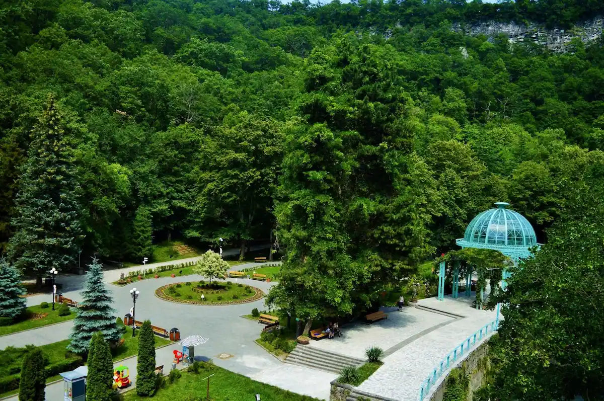 Aerial view of Borjomi Central Park in Georgia, featuring the historic Blue Pavilion mineral water spring and lush green forest.