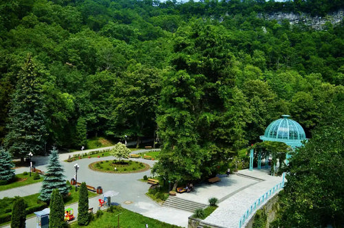 Aerial view of Borjomi Central Park in Georgia, featuring the historic Blue Pavilion mineral water spring and lush green forest.