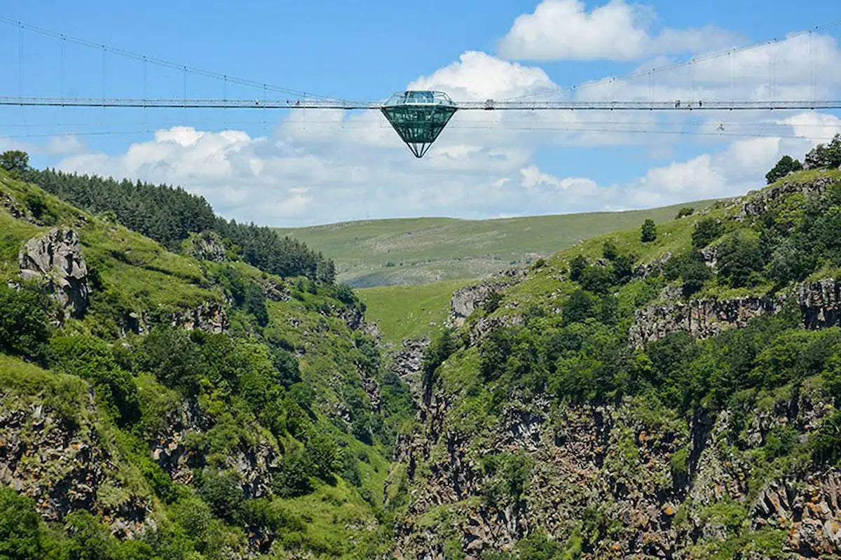 The Diamond Eye glass suspension bridge hanging over the lush green Dashbashi Canyon in Georgia, featuring a diamond-shaped panoramic platform
