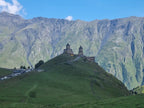 Wide landscape view of Gergeti Trinity Church perched on a green hill beneath the dramatic Caucasus mountains in Georgia