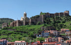View of Narikala Fortress and St. Nicholas Church on a green hill above the traditional colorful houses of Old Tbilisi