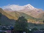 Stepantsminda village settlement nestled below the snow-capped Mount Kazbek peak during a private mountain tour in Georgia.